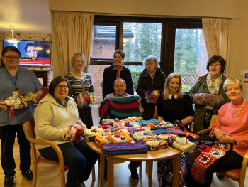 Omagh Carers Knitting Group pictured with a selection of beautifully hand knitted twiddle muffs and blankets donated to residents at Meadowbank Residential Home, Omagh standing from left to right: Clare Walsh, Care Worker, Meadowbank Residential Home; Joy Aiken; Clare Lafferty, Manager, Meadowbank Residential Home; Patricia O’Kane and Kathleen Donaghy. Seated from left to right: Kathryn Doherty; Tony Cassidy, Resident; Geraldine McLaughlin, Carers Support Worker, Western Trust and Beth Wylie.