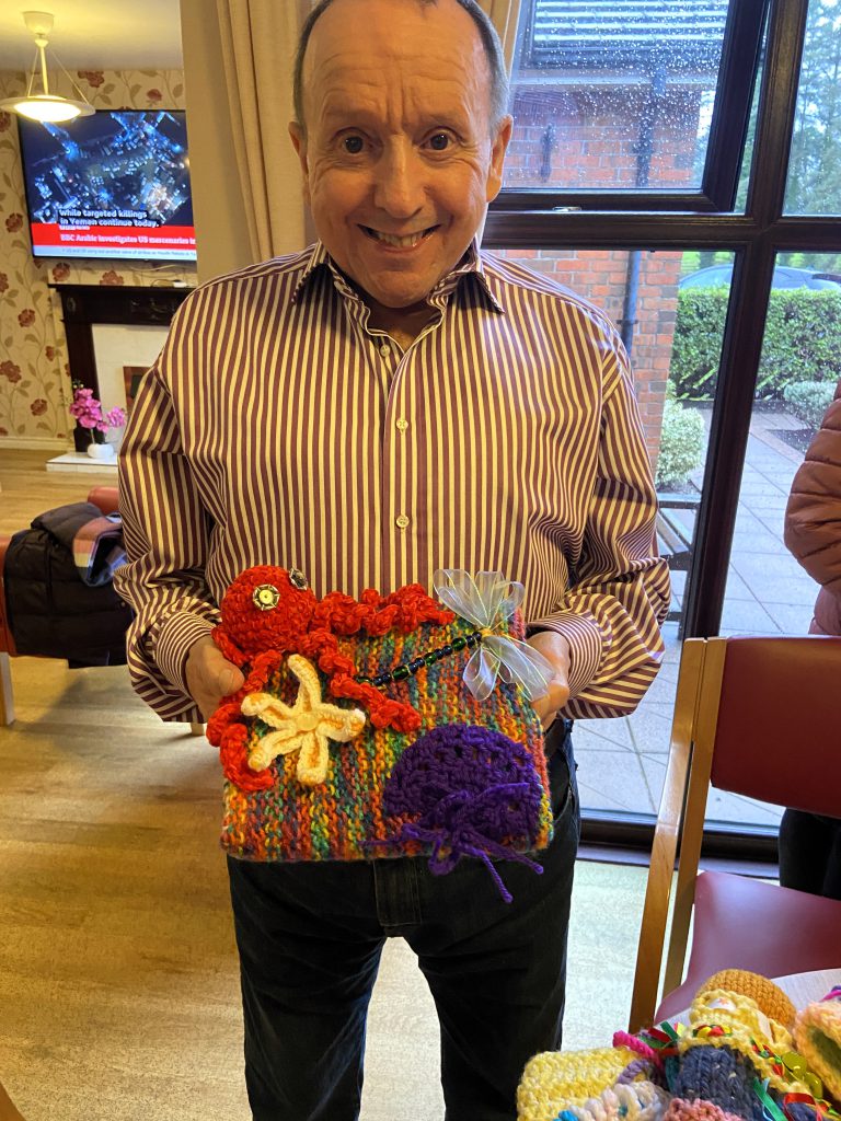 Tony Cassidy, Resident at Meadowbank Residential Home delighted with the beautifully hand knitted twiddle muff kindly donated by the Omagh Carers Knitting Group.