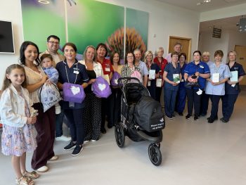 Group photo of family and maternity staff holding dignity pack and books with privacy pram in front of group
