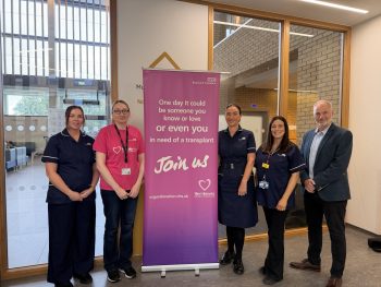 Staff with a NHS Blood and Transplant pop up banner - 'One day it could be someone you know or love or even you in need of a transplant. Join Us, organdonation.nhs.uk