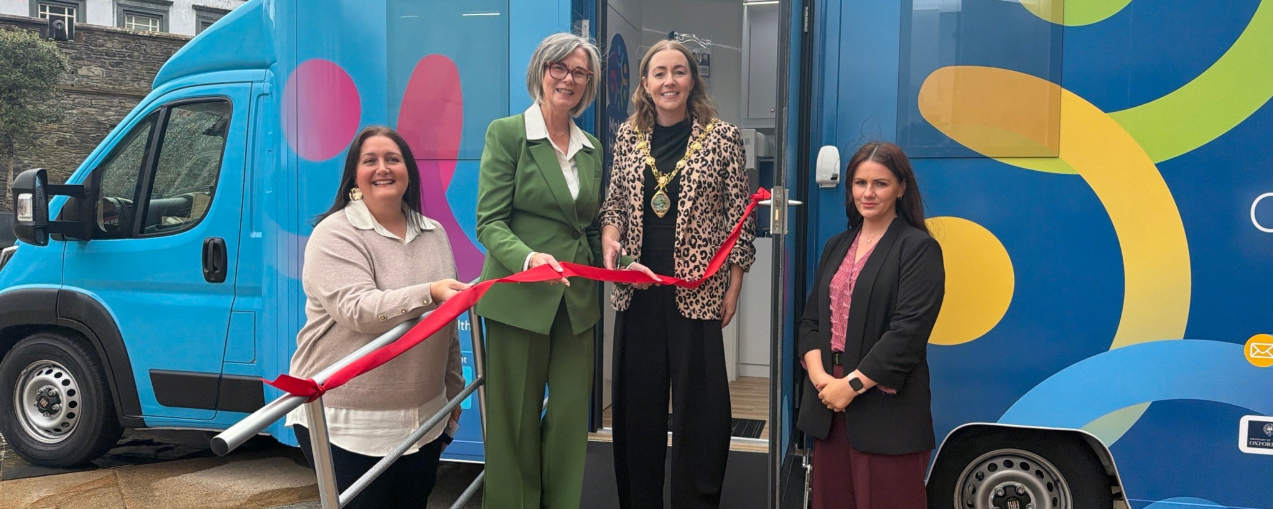 A group of women standing on a ramp with a ribbon in front of the new Research Bus NI