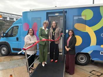A group of women standing on a ramp with a ribbon in front of the new Research Bus NI