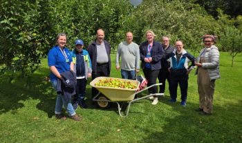 Group of representatives from the National Trust and Fresh Focus Day Opportunities in an orchard with trees and wheelborrow