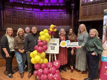 Large group of people standing with pink and yellow balloon arch and sign that displays the words "Adoption Week 2026"